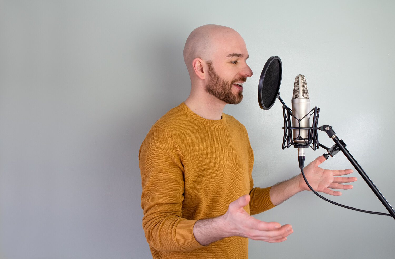 Bald headed man wearing his favourite mustard coloured jumper speaking closely into a professional microphone